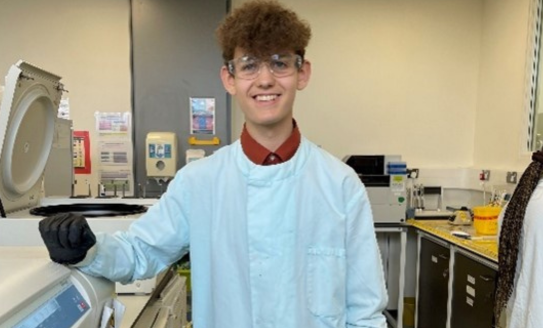 Young boy in lab coat smiling at camera.